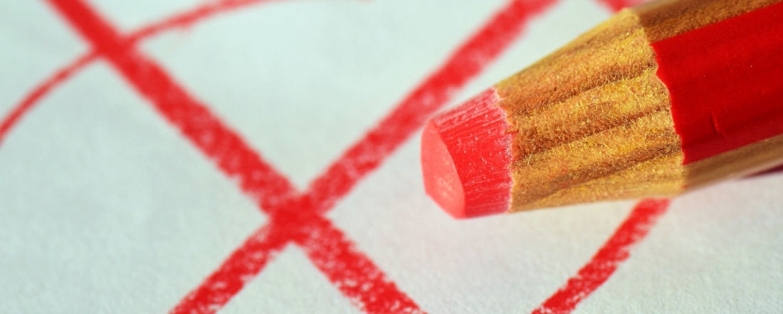 Ein roter Buntstift mit einem weißen Blatt mit einem roten angekreuzten Kreis im Hintergrung